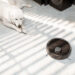 Dog laying next to robot vacuum.